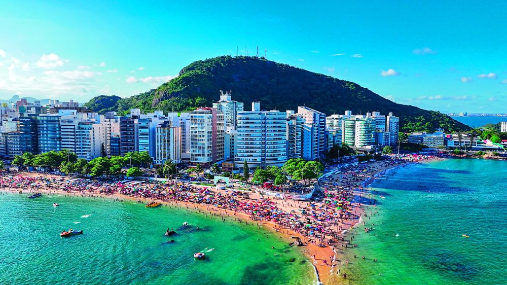 Aerial view of Praia da Costa full of beach umbrellas, with the seafront buildings and Morro do Moreno behind.