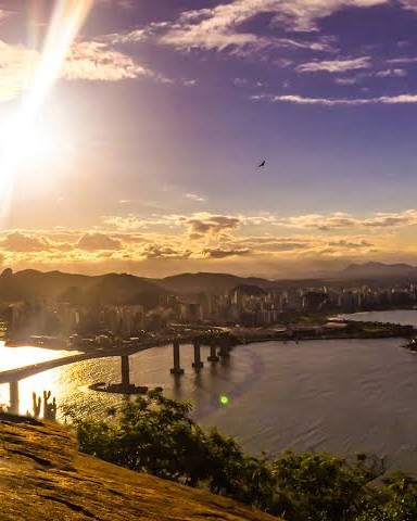 Sunset seen from high on a rock, golden light over the bay, the Terceira Ponte bridge and the city beyond.